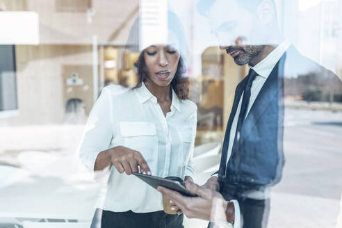 Serious male and female business professionals seen through glass while discussing in office - JSRF01526