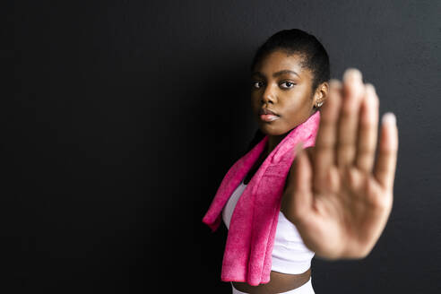 Selbstbewusste Frau mit Stopp-Geste im Stehen vor schwarzem Hintergrund - GIOF12547
