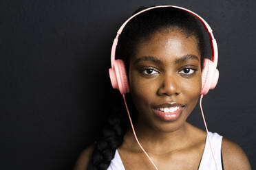 Lächelnde Frau hört Musik über Kopfhörer vor schwarzem Hintergrund - GIOF12549