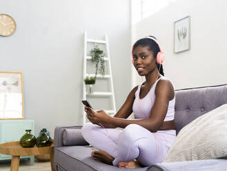 Smiling woman wearing headphones while using mobile phone at home - GIOF12597