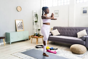 Junge Frau, die auf einem Bein steht, während sie zu Hause Yoga macht - GIOF12604
