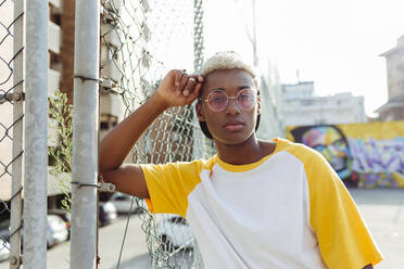 Hübscher junger schwarzer Mann liegt auf einem Zaun auf der Straße und schaut in die Kamera - ADSF23820
