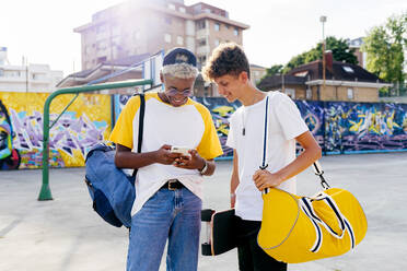 Zwei Teenager mit Skateboard und Rucksack telefonieren auf der Straße - ADSF23821