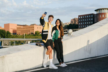 Ein paar Teenager sitzen auf der Mauer und machen ein Selfie mit dem Handy auf der Straße - ADSF23824