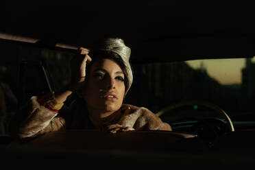 Trendige Frau mit Blume auf dem Hut im Auto, die wegschaut - ADSF23866