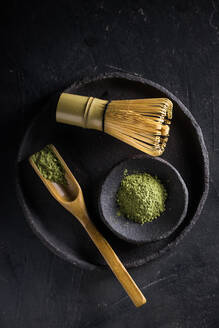 Spoon with dried matcha tea leaves on black tableware with chasen for traditional oriental ceremony - ADSF23896