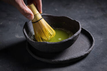 Von oben: die Hand hält den traditionellen japanischen Matcha mit einem Teebesen in einer Steinschale für eine traditionelle orientalische Zeremonie - ADSF23898