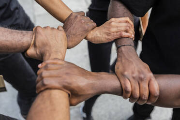 From above of crop anonymous African American partners holding hands demonstrating unity symbol in town - ADSF23910