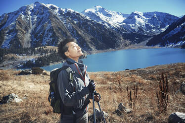 Woman with eyes closed standing at mountain lake - AZF00313