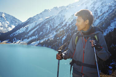 Woman wearing backpack looking away while holding hiking poles by mountain - AZF00315