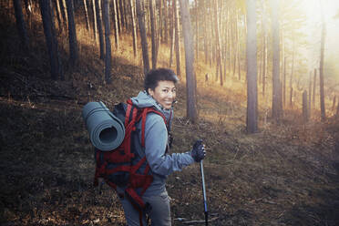 Lächelnde Frau mit Rucksack schaut über die Schulter beim Wandern im Wald - AZF00322