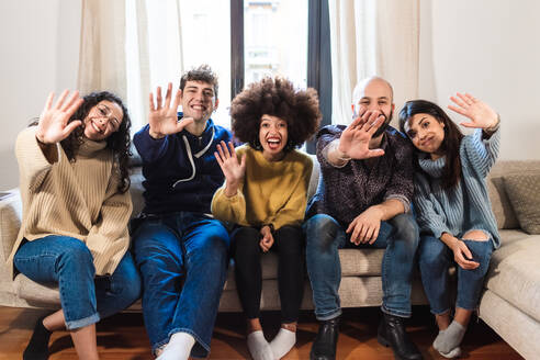 Friends sitting on sofa, waving on video call - ISF24377