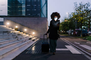 Businesswoman walking with suitcase, wearing face mask - ISF24384