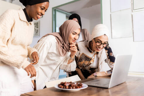 Junge muslimische Frauen bei einem Videoanruf, mit einem Teller voller Datteln - ISF24437