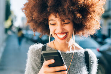 Young woman looking at phone outdoors, smiling - ISF24456