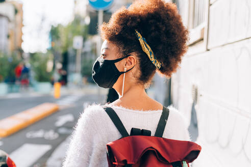 Young woman walking in city, wearing face mask, rear view - ISF24463