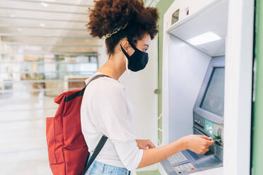 Young woman wearing face mask, using ATM - ISF24470