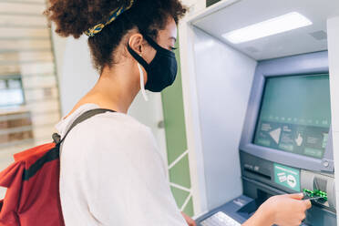 Young woman wearing face mask, using ATM - ISF24471