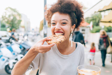 Junge Frau isst Keks in einem Straßencafé - ISF24474