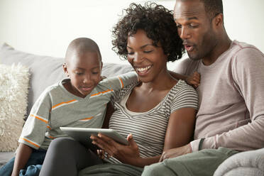 Boy with parents on sofa using digital tablet - ISF24510