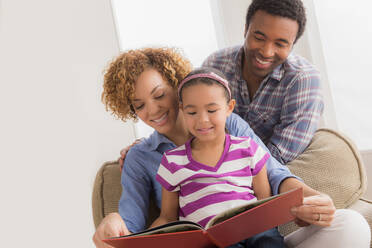Eltern mit Tochter beim Lesen eines Buches - ISF24554