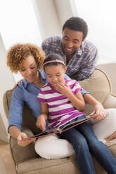 Eltern mit Tochter beim Lesen eines Buches - ISF24555