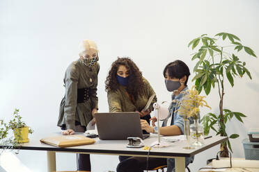 Colleagues looking at laptop, wearing face masks - ISF24572