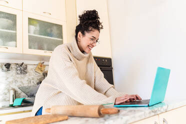 Young woman looking at laptop in kitchen - ISF24598