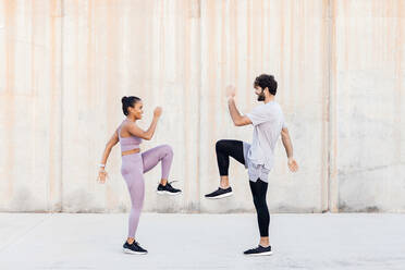 Side view of young determined diverse athletes in sportswear exercising and looking at each other - ADSF23914