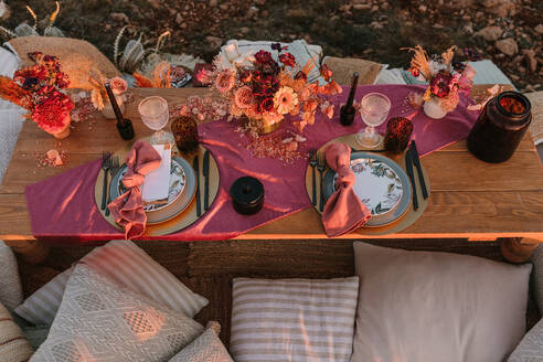 Von oben von hölzernen Tisch mit Besteck auf Platten serviert auf Tuch in der Nähe bunte Blumensträuße mit Weingläsern während der Hochzeitsfeier - ADSF23918