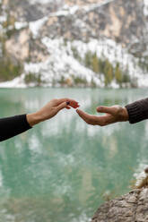 Crop anonymous traveler holding hand with girlfriend while supporting for climbing on rocky shore of Lago di Braies lake in Italy - ADSF23949