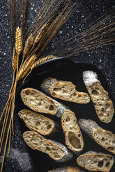 From above of appetizing crusty bread near wheat spikes and dark fabric on table - ADSF23969