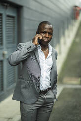 Adult African American businessman in stylish suit talking on cellphone while looking away in city - ADSF24044