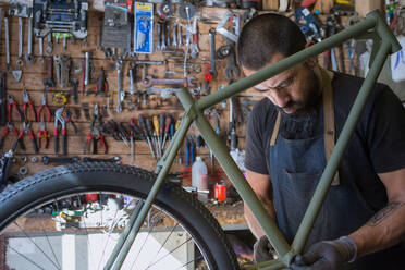 Male mechanic in gloves repairing bicycle in modern workshop - ADSF24061
