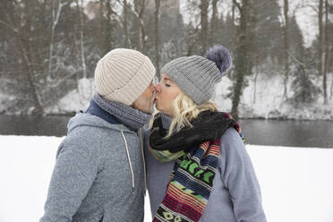 Senior couple kissing while standing at park during winter - FVDF00140