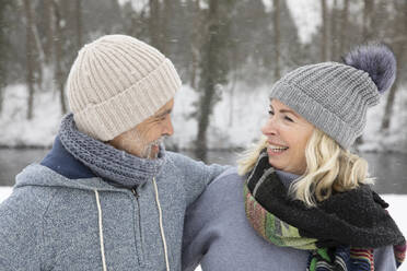 Happy senior couple in warm clothing looking at each other during winter - FVDF00142