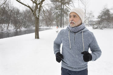 Älterer Mann schaut beim Laufen im Park im Winter weg - FVDF00160