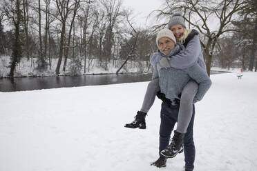 Man piggybacking playful woman while standing on snow - FVDF00166
