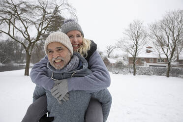 Senior man piggybacking woman at park during winter - FVDF00168