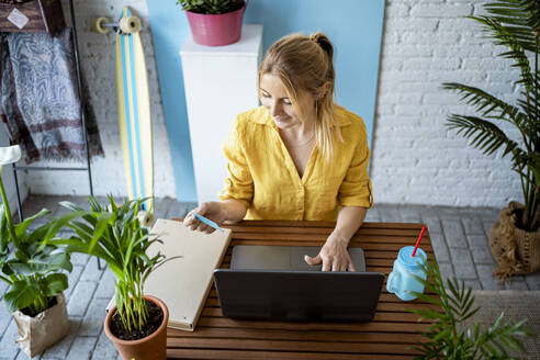 Female professional holding credit card while using laptop on desk at home office - RCPF01020