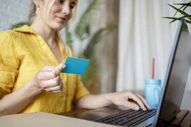 Eine Unternehmerin hält eine Kreditkarte in der Hand, während sie im Büro zu Hause am Laptop arbeitet - RCPF01022