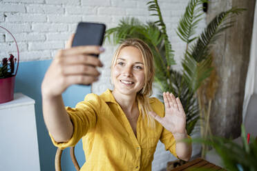 Weibliche Fachkraft winkt während eines Videogesprächs mit einem Smartphone im Büro zu Hause - RCPF01028