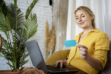 Businesswoman with laptop while shopping through credit card at home - RCPF01034