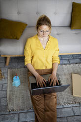Geschäftsfrau, die zu Hause sitzend am Laptop arbeitet - RCPF01042