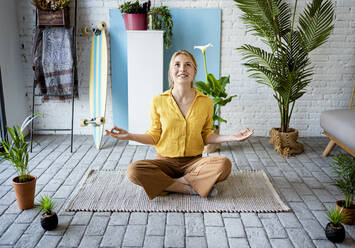 Young woman meditating while sitting on mat at home - RCPF01054