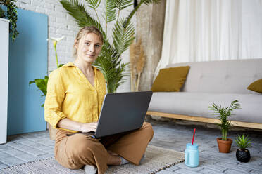 Female professional working on laptop while sitting on mat at home - RCPF01055