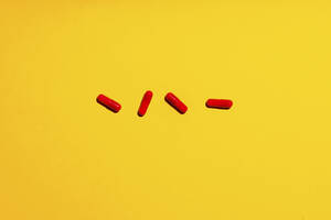 Vier rote Arzneimittelkapseln auf gelbem Hintergrund - GEMF04765