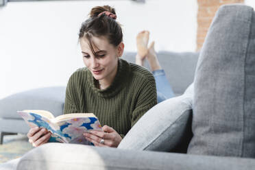 Woman reading book on sofa at home - MCVF00783