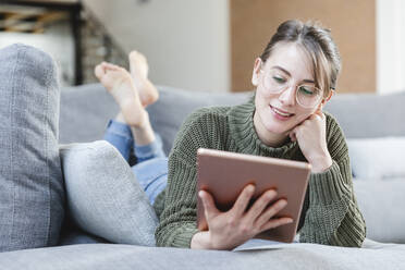 Frau mit Brille benutzt digitales Tablet auf dem Sofa zu Hause - MCVF00784