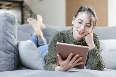 Woman with eyeglasses using digital tablet on sofa at home - MCVF00784